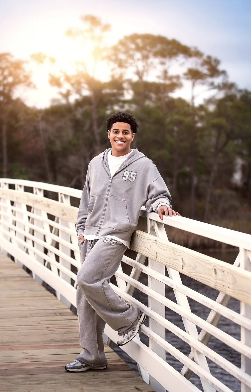 A senior portrait on a white footbridge, warm light through the trees